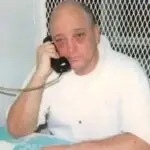 man on death row in white clothing talking on phone