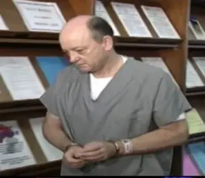 prisoner in handcuffs walking by shelf with stacks of paper